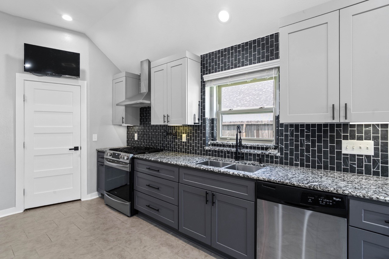 12126 Walden Road Montgomery, TX 77356 - Photo 31 of 50 Stunning remodeled kitchen featuring custom cabinetry, beautiful granite countertops, and a striking full-height tile backsplash that adds modern style and character. Enjoy cooking on the upgraded gas range with a sleek vent hood, all while staying connected with the mounted TV that stays with the home. This kitchen also offers a spacious walk-in pantry for exceptional storage and organization. A perfect blend of function and design, ideal for everyday living and entertaining.