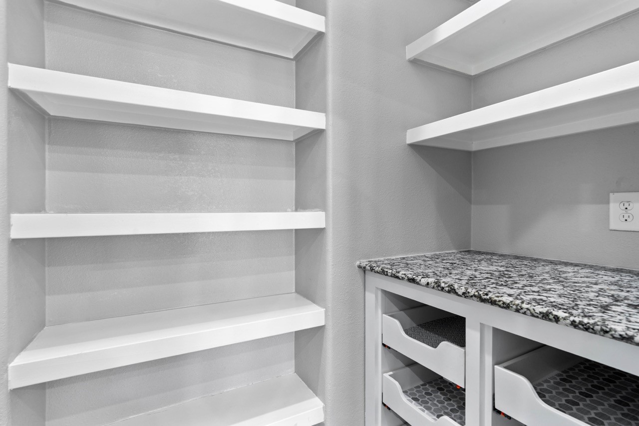 12126 Walden Road Montgomery, TX 77356 - Photo 32 of 50 Spacious walk-in pantry featuring built-in shelving for maximum storage and organization. Granite countertop offers additional prep space, while lower pull-out drawers provide easy access to kitchen essentials. Fresh neutral finishes and ample shelving make this pantry both functional and beautifully designed for everyday convenience.