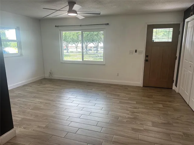 an empty room with wooden floor chandelier fan and windows