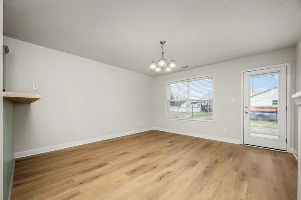 an empty room with wooden floor chandelier and windows