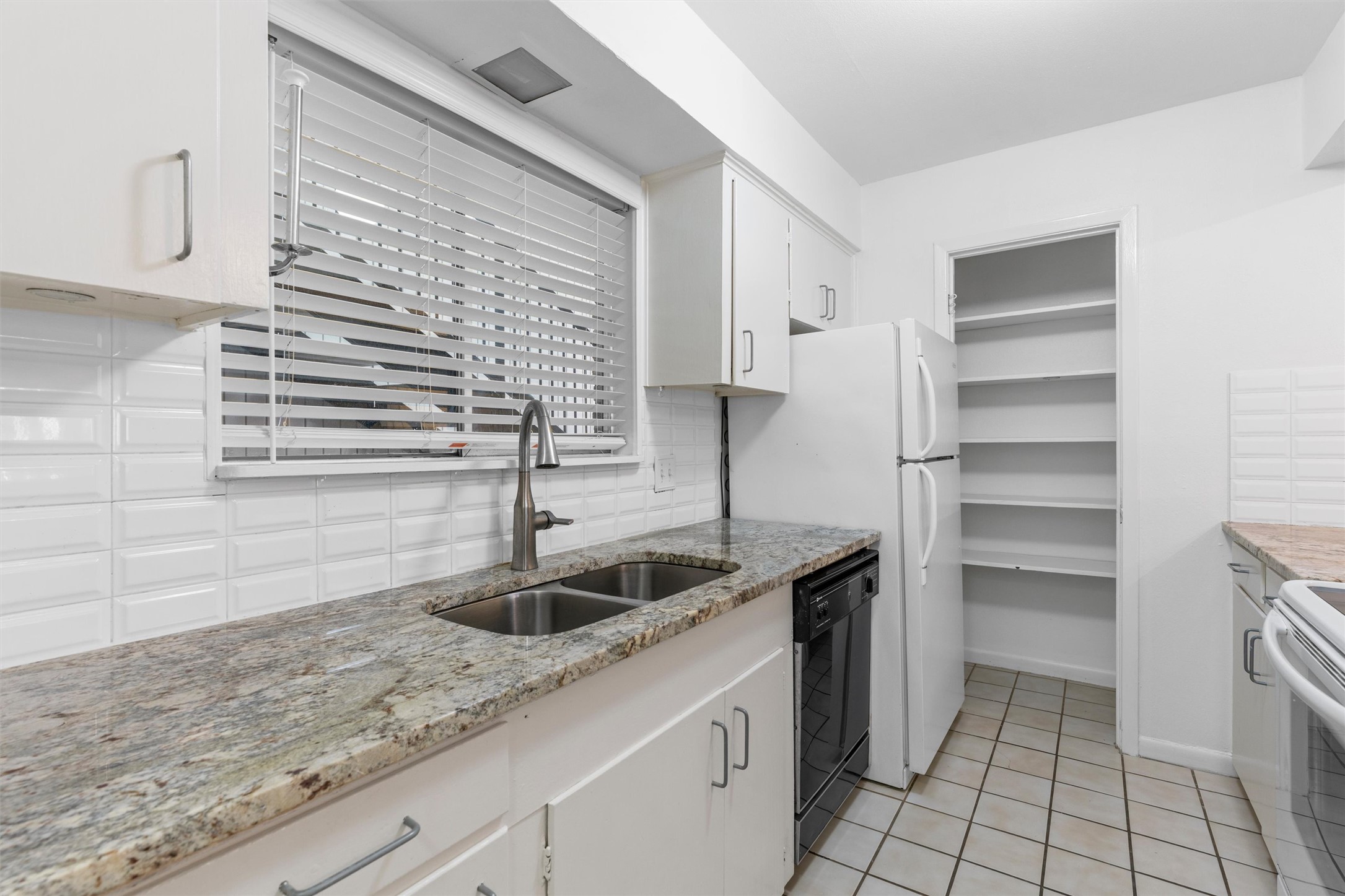 2208 Enfield Road, Unit 10500 Austin, TX 78703 - Photo 17 of 34 Kitchen featuring white cabinetry, a double basin stainless steel sink with a high-arc faucet, granite countertops, and a white subway tile backsplash