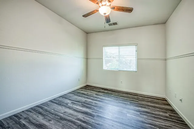 an empty room with wooden floor fan and windows