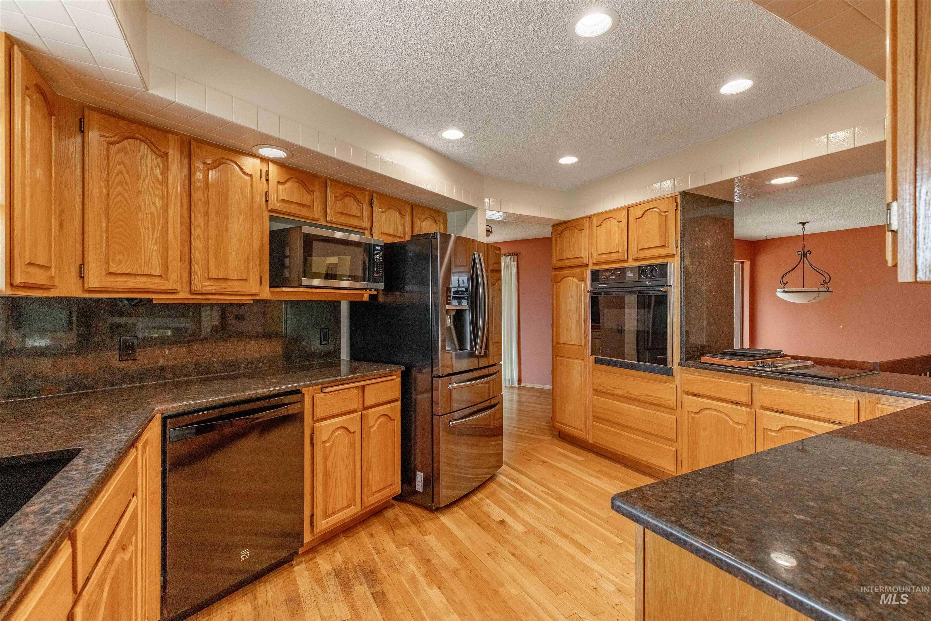 1050 Paradise Ridge Road Moscow, ID 83843 - Photo 11 of 49 Kitchen featuring a textured ceiling, black appliances, light wood-style flooring, wood finish cabinetry, and tasteful backsplash