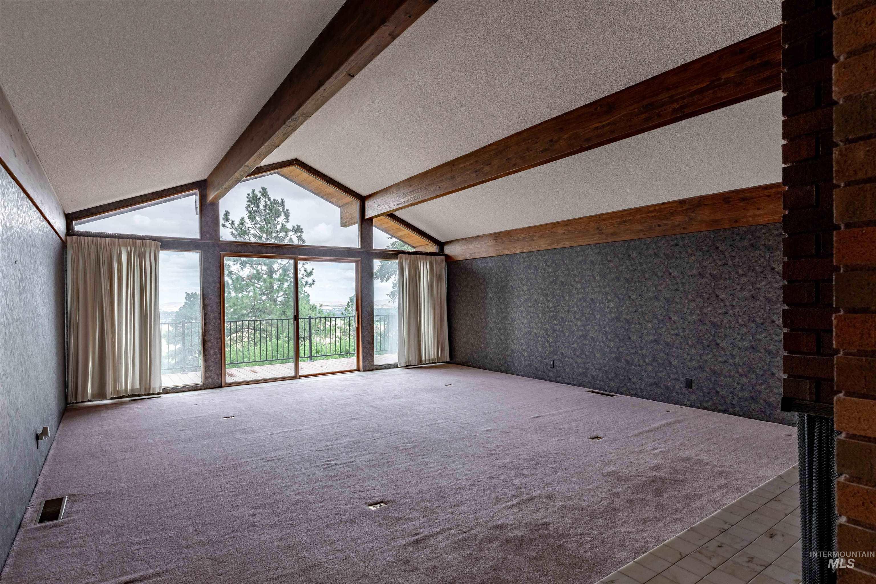 1050 Paradise Ridge Road Moscow, ID 83843 - Photo 14 of 49 Unfurnished living room featuring wallpapered walls, beam ceiling, floor to ceiling windows, and carpet floors