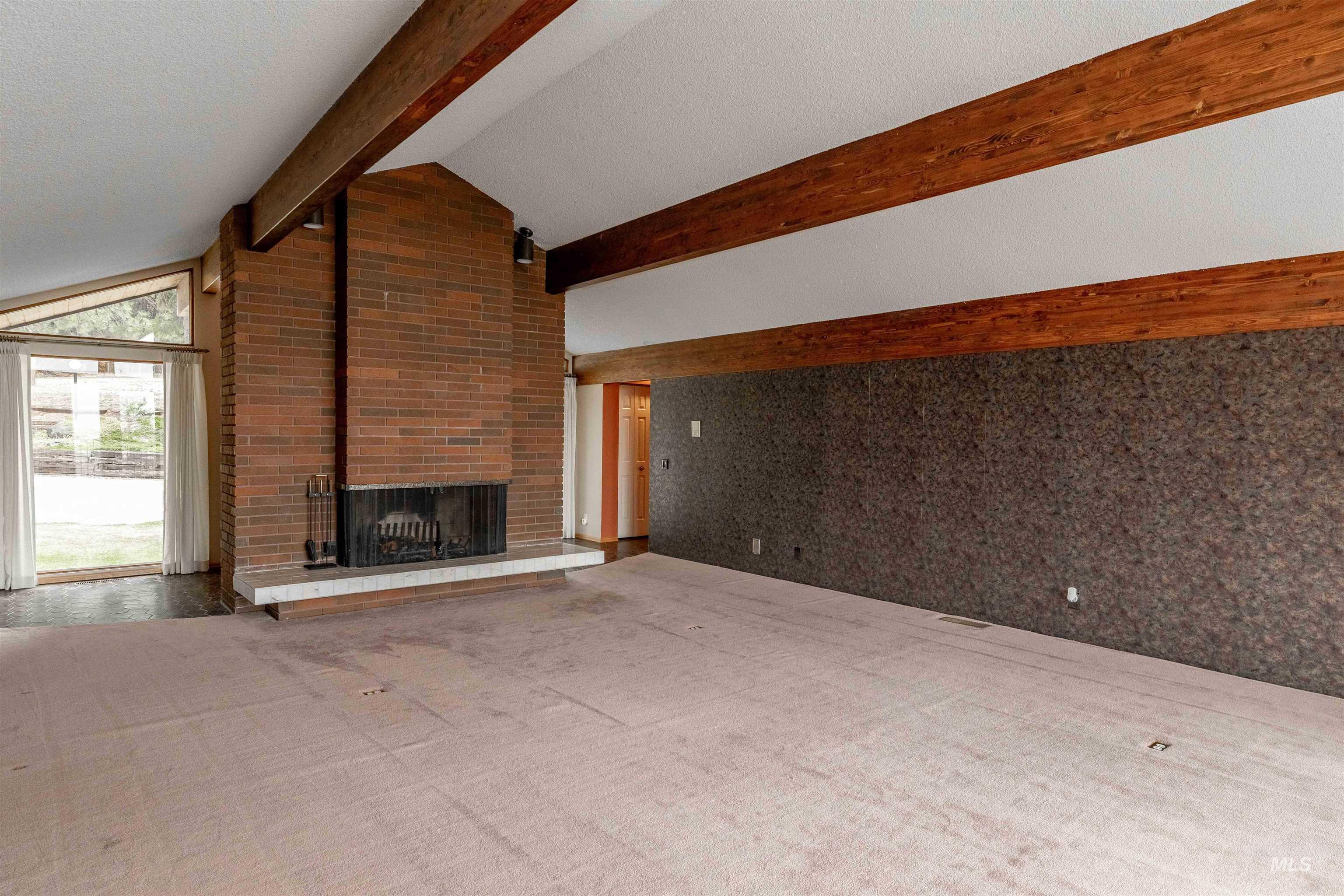 1050 Paradise Ridge Road Moscow, ID 83843 - Photo 15 of 49 Unfurnished living room featuring beamed ceiling, carpet floors, a brick fireplace, and a textured ceiling