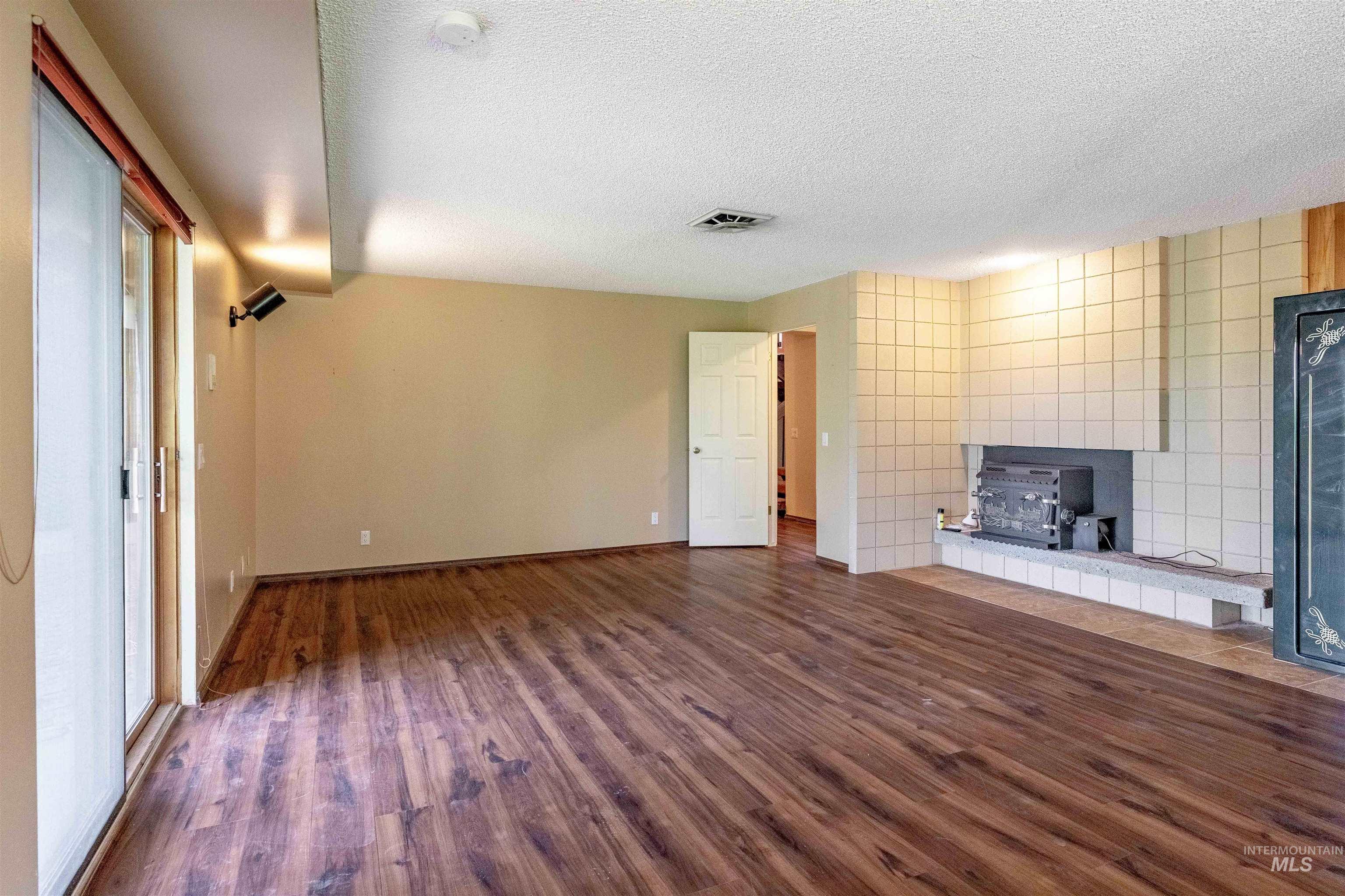 1050 Paradise Ridge Road Moscow, ID 83843 - Photo 28 of 49 Unfurnished living room featuring dark wood-type flooring, a textured ceiling, a wood stove, and tile walls