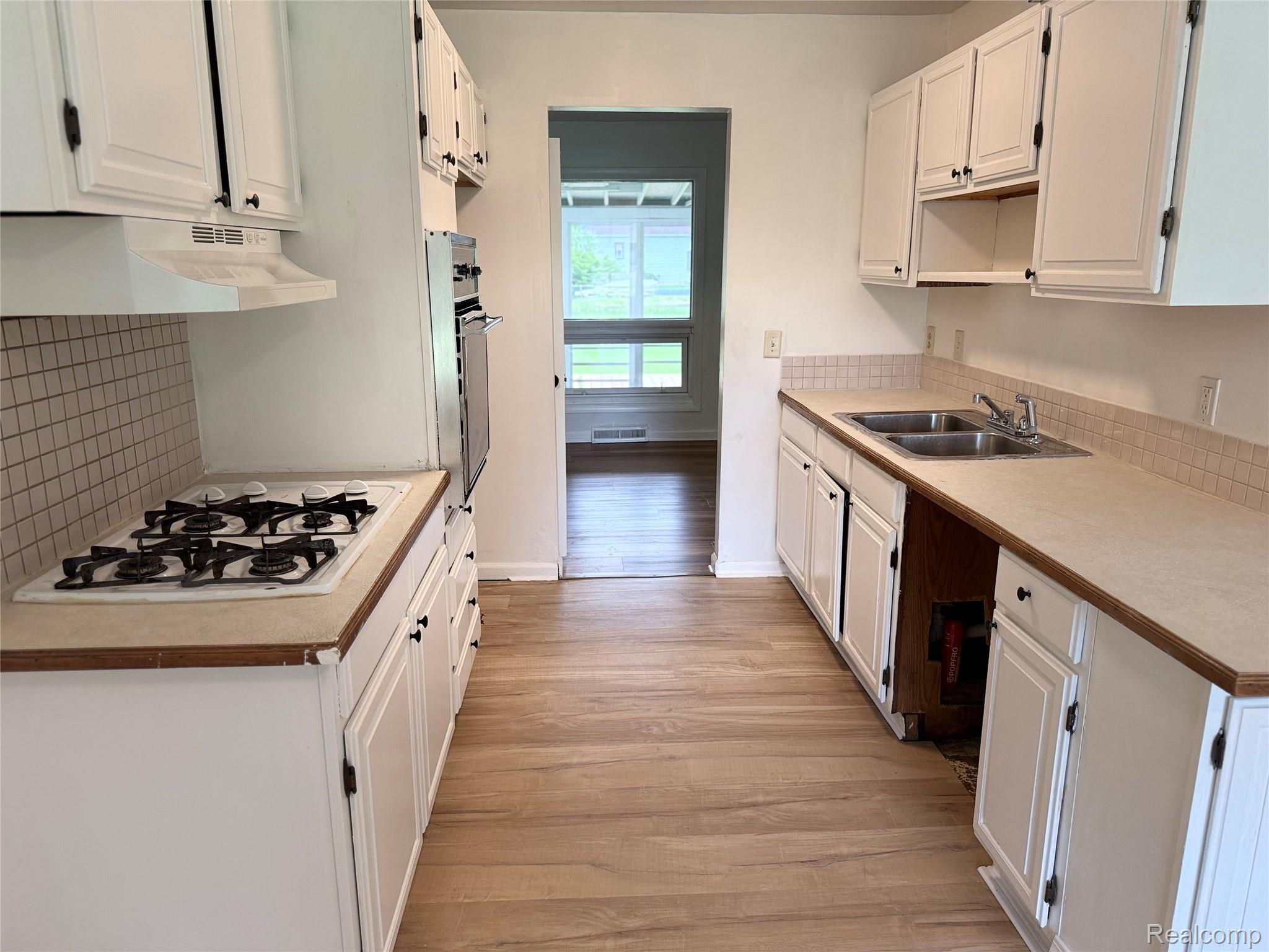 5347 Mapletree Drive Flint, MI 48532 - Photo 4 of 10 Kitchen featuring white cabinetry, light wood-finish flooring, a double basin stainless steel sink, a gas range with overhead ventilation, and a built-in oven