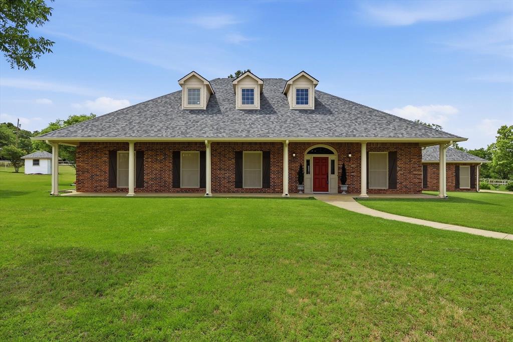 6955 Hawk Road Flower Mound, TX 75022 - Photo 1 of 40 Brick exterior residence featuring a covered front porch with white columns, a red entry door, a gray shingle roof, and three dormer windows