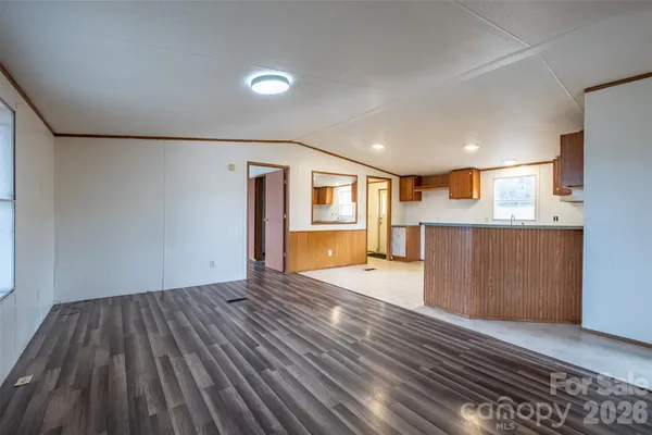 a view of empty room with wooden floor and kitchen