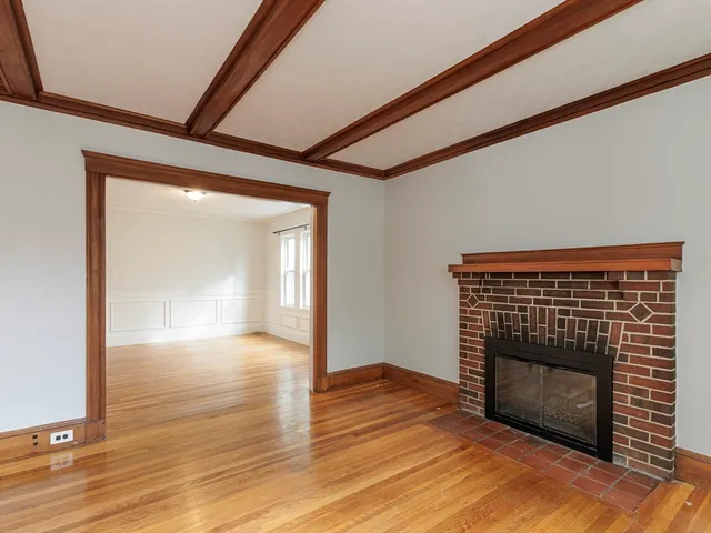 a view of an empty room with wooden floor fireplace and a window