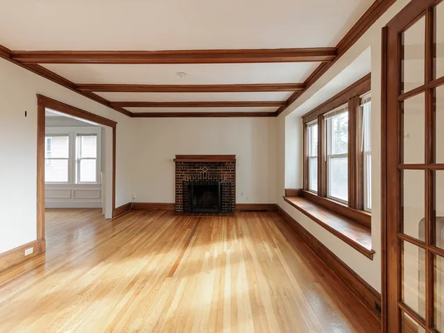 a view of an empty room with wooden floor fireplace and a window