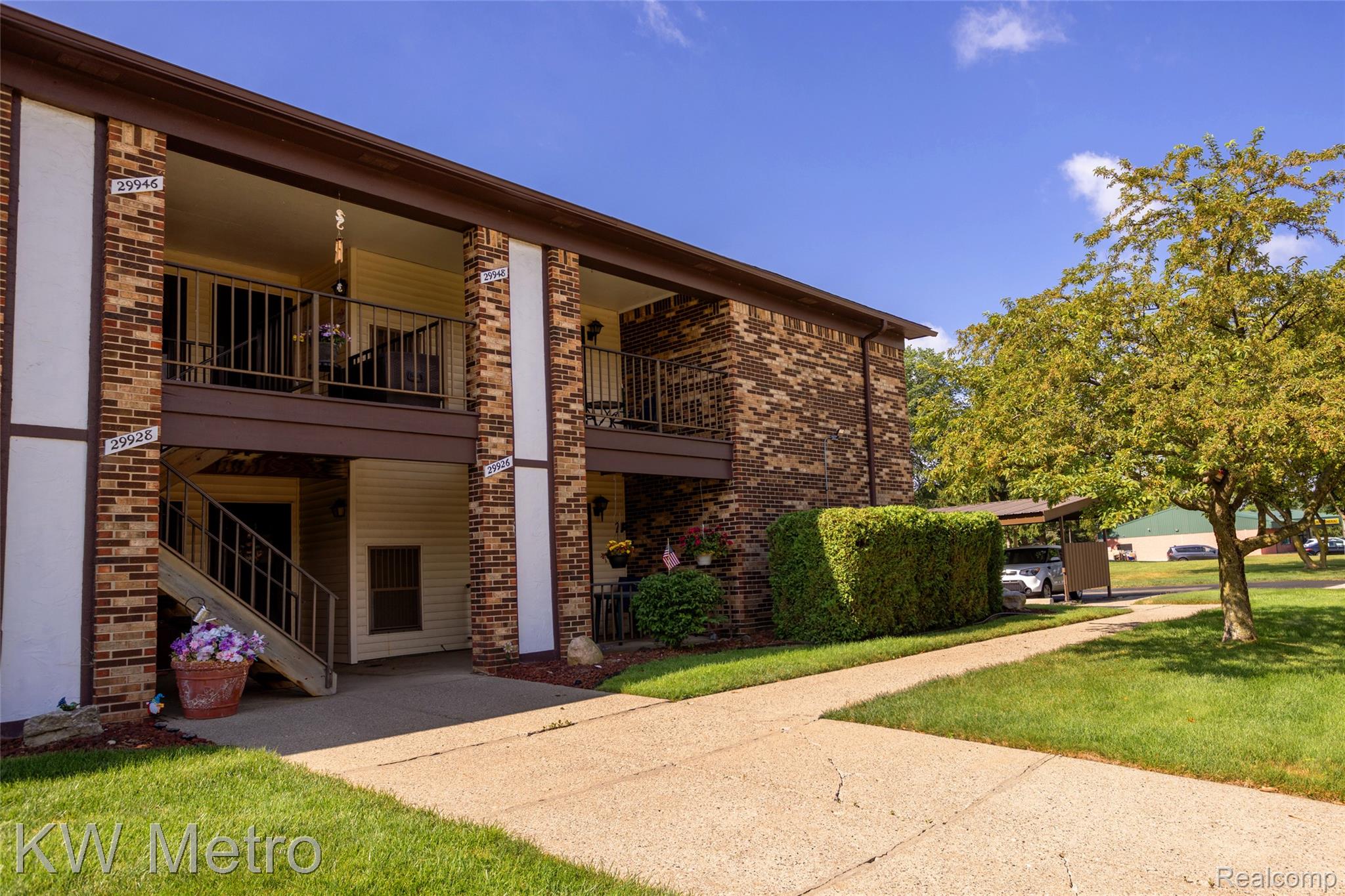 29948 Utica Road Roseville, MI 48066 - Photo 12 of 12 Brick and siding exterior featuring balconies, an exterior staircase with metal railings, a paved walkway, and a covered parking area