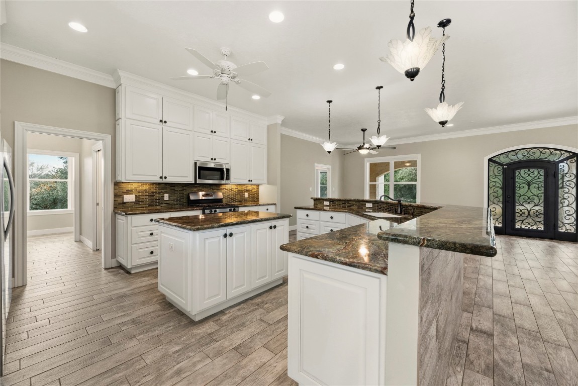 2051 Hillview Road Bellville, TX 77418 - Photo 16 of 47 Gourmet island kitchen features white cabinetry, glass tile backsplash, marble countertops, under cabinet lighting, stainless steel appliances, gas range, lovely pendant lighting and a large breakfast bar with seating up to 8.