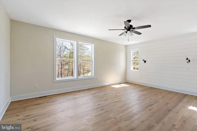 an empty room with wooden floor fan and windows