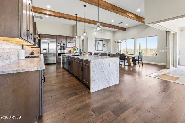 a kitchen with stainless steel appliances granite countertop a stove top oven a sink a dining table and chairs with wooden floor