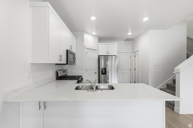 1173 West 1870 South Logan, UT 84321 - Photo 6 of 33 Modern kitchen featuring white cabinetry, light-toned countertops, stainless steel appliances, and an integrated kitchen island with a sink