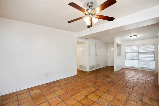 an empty room with chandelier fan and windows