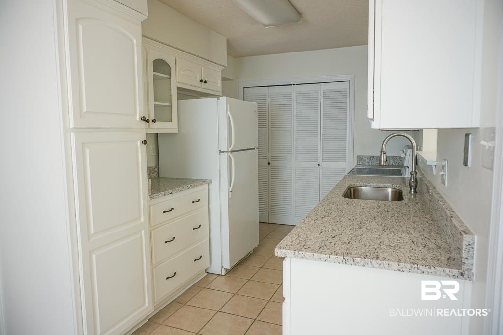 4377 Fathbrook Lane Mobile, AL 36693 - Photo 9 of 19 Kitchen featuring light stone countertops, glass insert cabinets, a sink, light tile patterned floors, and freestanding refrigerator