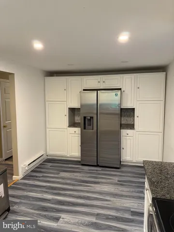 a view of a refrigerator in kitchen and an empty room with wooden floor