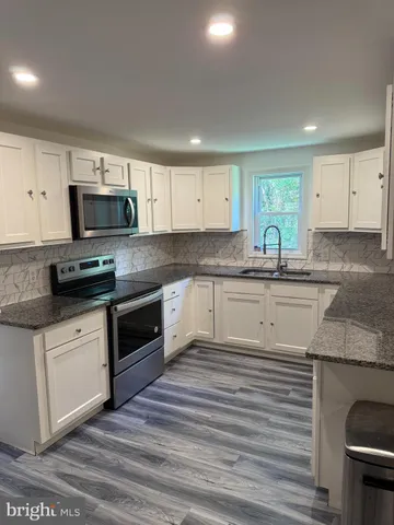 a kitchen with granite countertop a sink stainless steel appliances and white cabinets