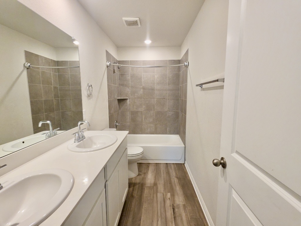 110 Grapefruit Road Hutto, TX 78634 - Photo 21 of 28 Bathroom featuring a dual vanity with undermount sinks, wood-finish flooring, tiled bath/shower combination with an integrated niche, and a full-width mirror