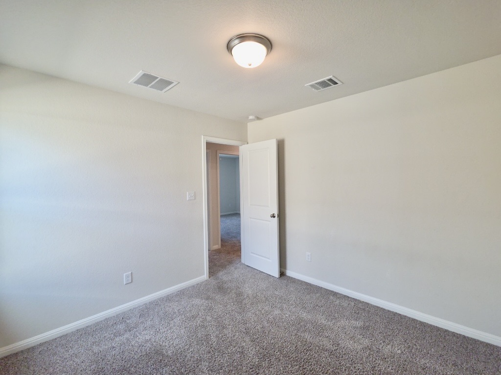 110 Grapefruit Road Hutto, TX 78634 - Photo 23 of 28 Neutral-toned room featuring a flush-mount ceiling light fixture, textured walls, and light gray carpet flooring