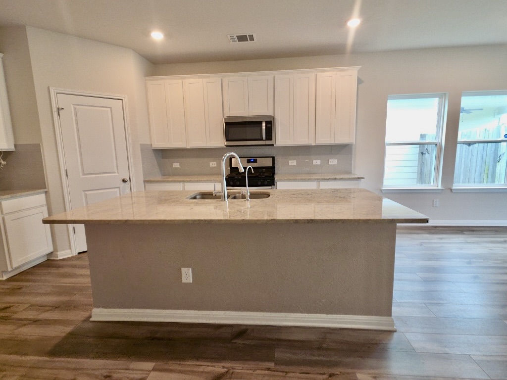 110 Grapefruit Road Hutto, TX 78634 - Photo 5 of 28 Kitchen island with a double basin sink, chrome gooseneck faucet, and light-toned countertop