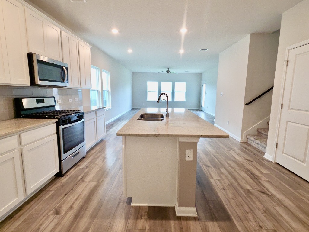 110 Grapefruit Road Hutto, TX 78634 - Photo 6 of 28 Kitchen featuring an expansive island with an undermount sink, light-toned countertops, white cabinetry, stainless steel appliances, and wood-finish flooring