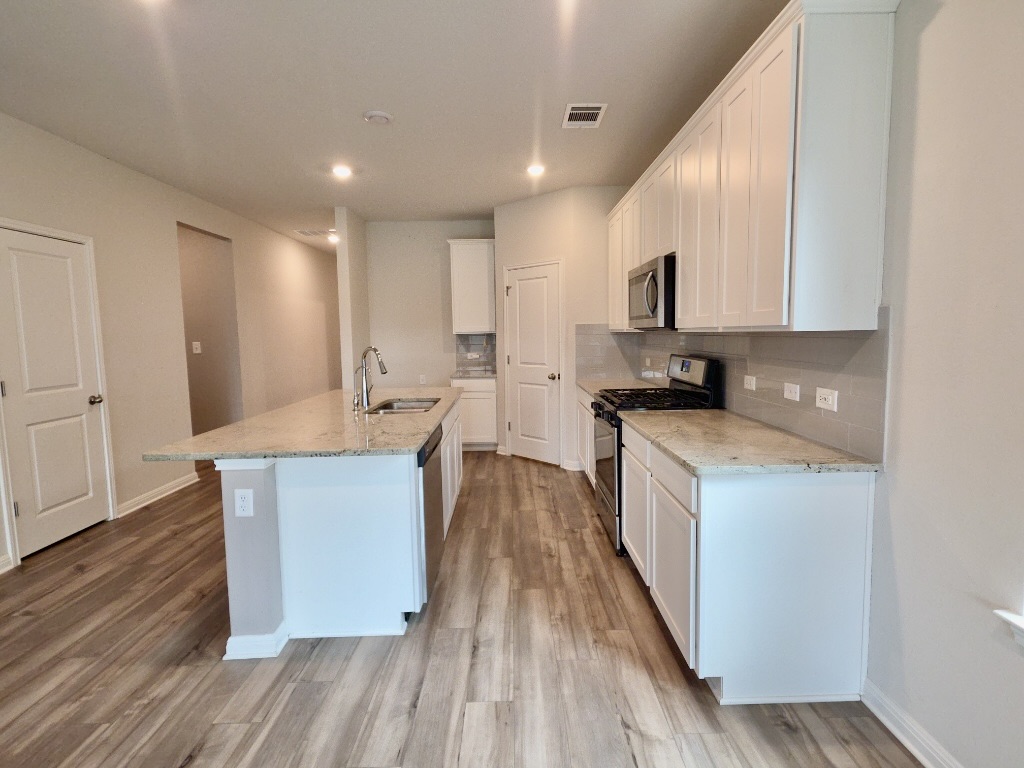 110 Grapefruit Road Hutto, TX 78634 - Photo 7 of 28 Contemporary kitchen featuring light wood-finish flooring, white cabinetry, stainless steel appliances, a light-toned countertop, and recessed lighting