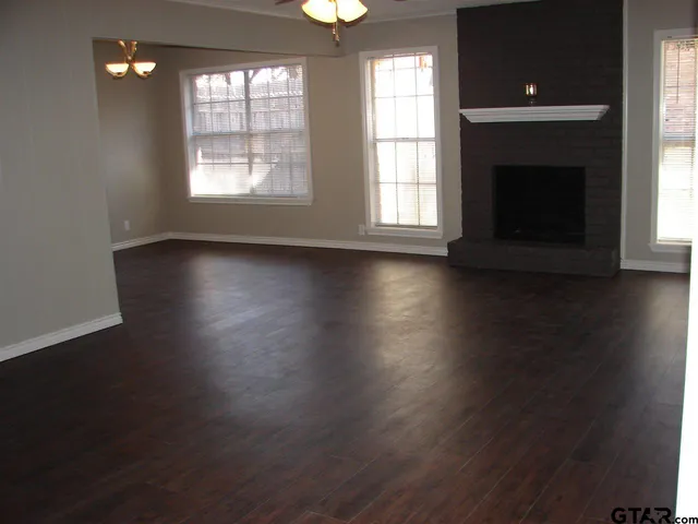 an empty room with wooden floor fireplace and windows