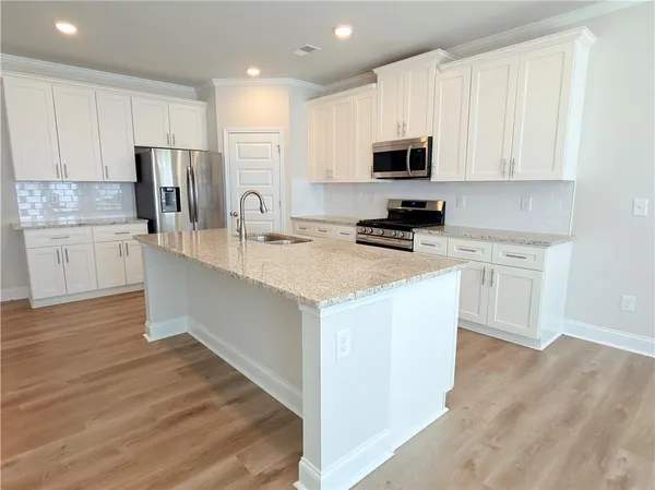 a kitchen with stainless steel appliances a microwave a stove a sink dishwasher a refrigerator and white cabinets with wooden floor