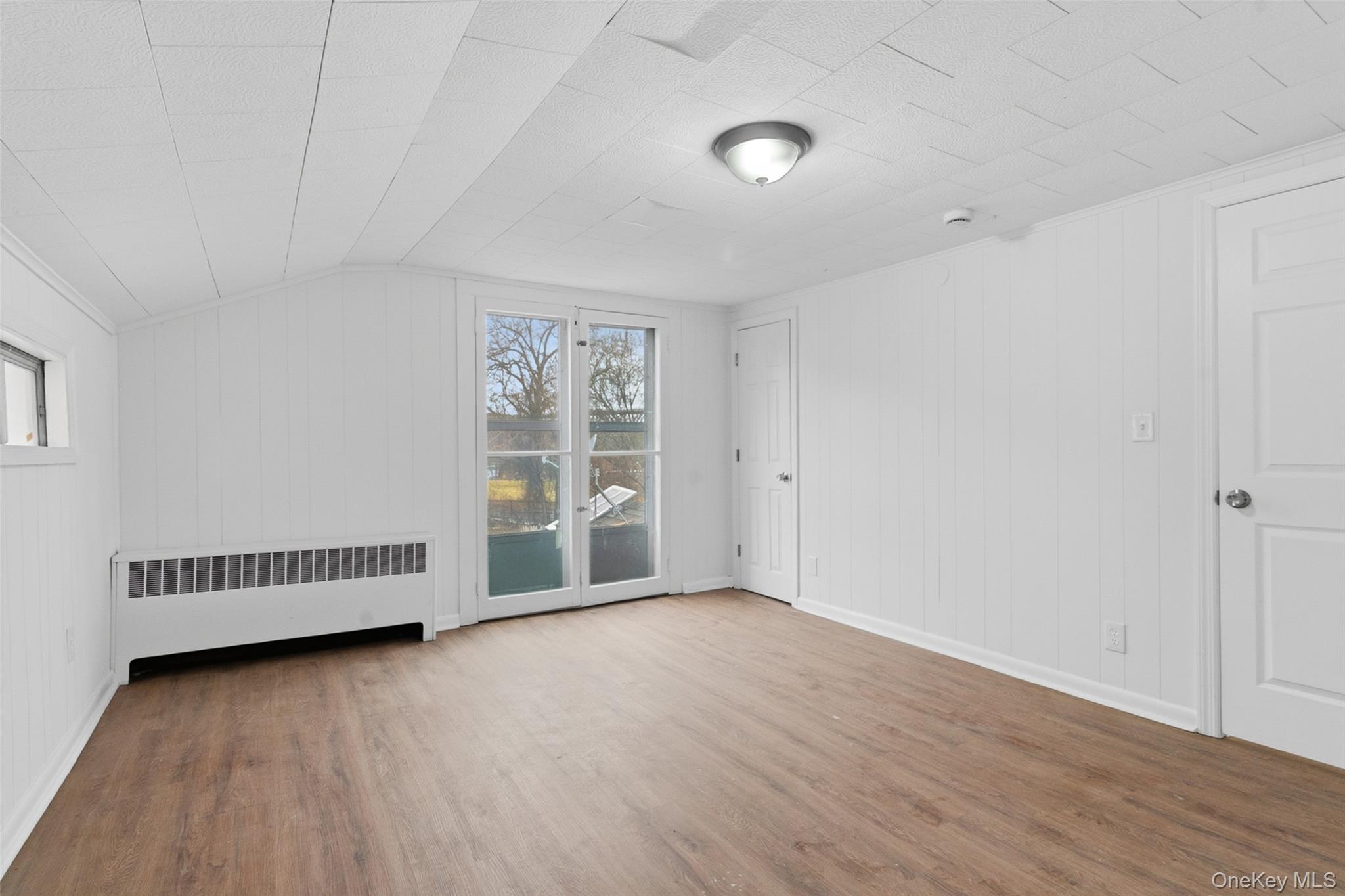 32 North Clover Street Poughkeepsie, NY 12601 - Photo 11 of 20 Empty room with radiator, wood finished floors, wood walls, and vaulted ceiling