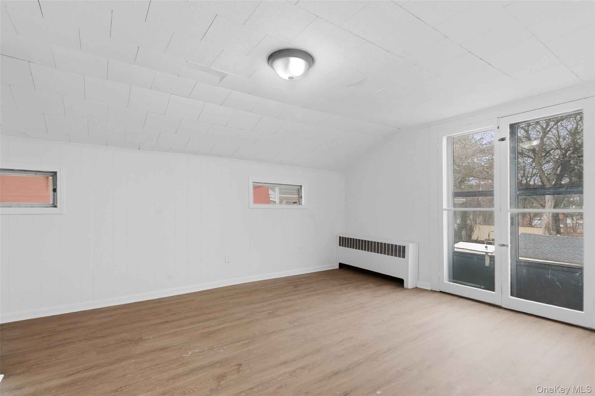 32 North Clover Street Poughkeepsie, NY 12601 - Photo 13 of 20 Additional living space featuring radiator, light wood-type flooring, vaulted ceiling, and wood walls