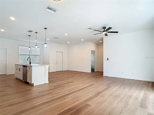 a view of an empty room with wooden floor and a ceiling fan