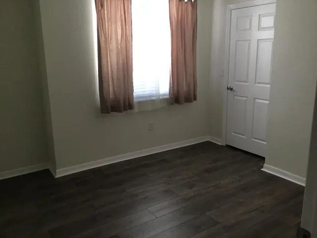 an empty room with wooden floor and windows with curtains