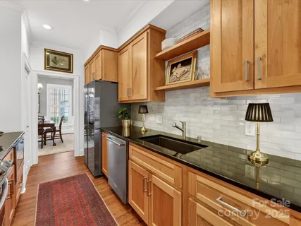 a kitchen with stainless steel appliances granite countertop a refrigerator a sink dishwasher a stove and a dining table with wooden floor