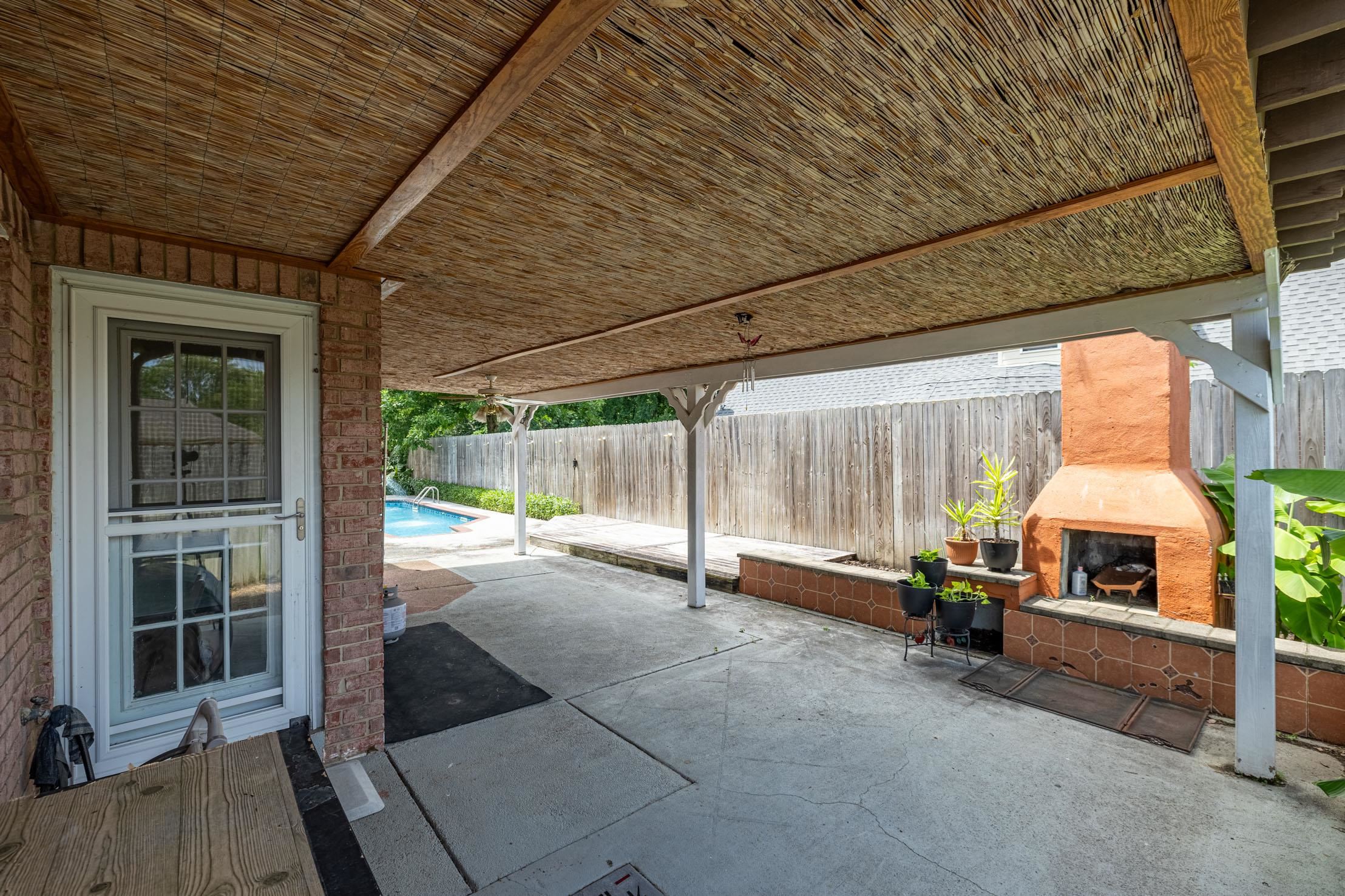 96 Berryfield Cove Collierville, TN 38017 - Photo 34 of 39 Covered patio featuring a wood-beam and bamboo-textured ceiling, a large concrete surface, an outdoor brick fireplace with a tile hearth, and a pool in the background