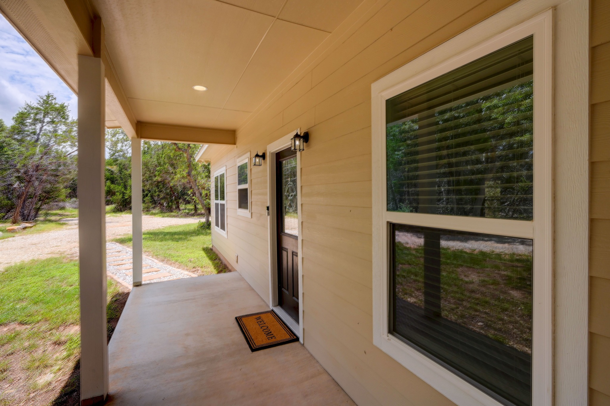 231 North Rainbow Ranch Road Wimberley, TX 78676 - Photo 5 of 40 A welcoming covered porch with sleek outdoor lighting fronts a serene, tree-lined landscape.