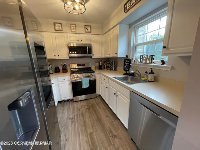 a kitchen with stainless steel appliances a sink a stove a refrigerator cabinets and a window