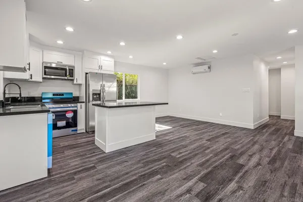 an empty room with wooden floor and a kitchen