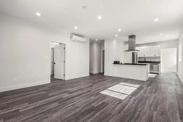 an empty room with kitchen view and wooden floor