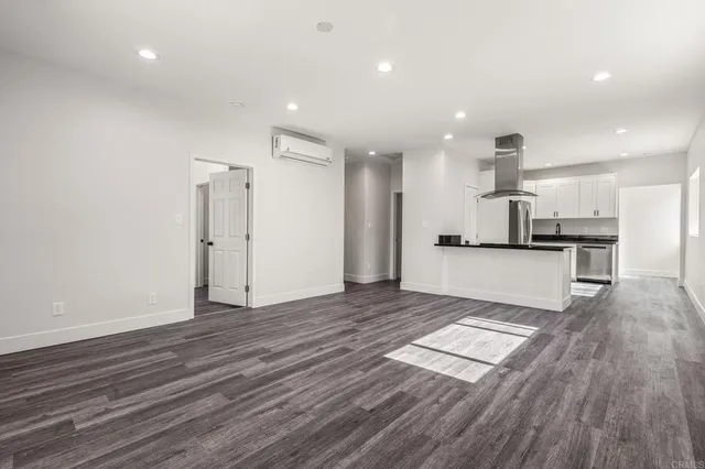 an empty room with kitchen view and wooden floor
