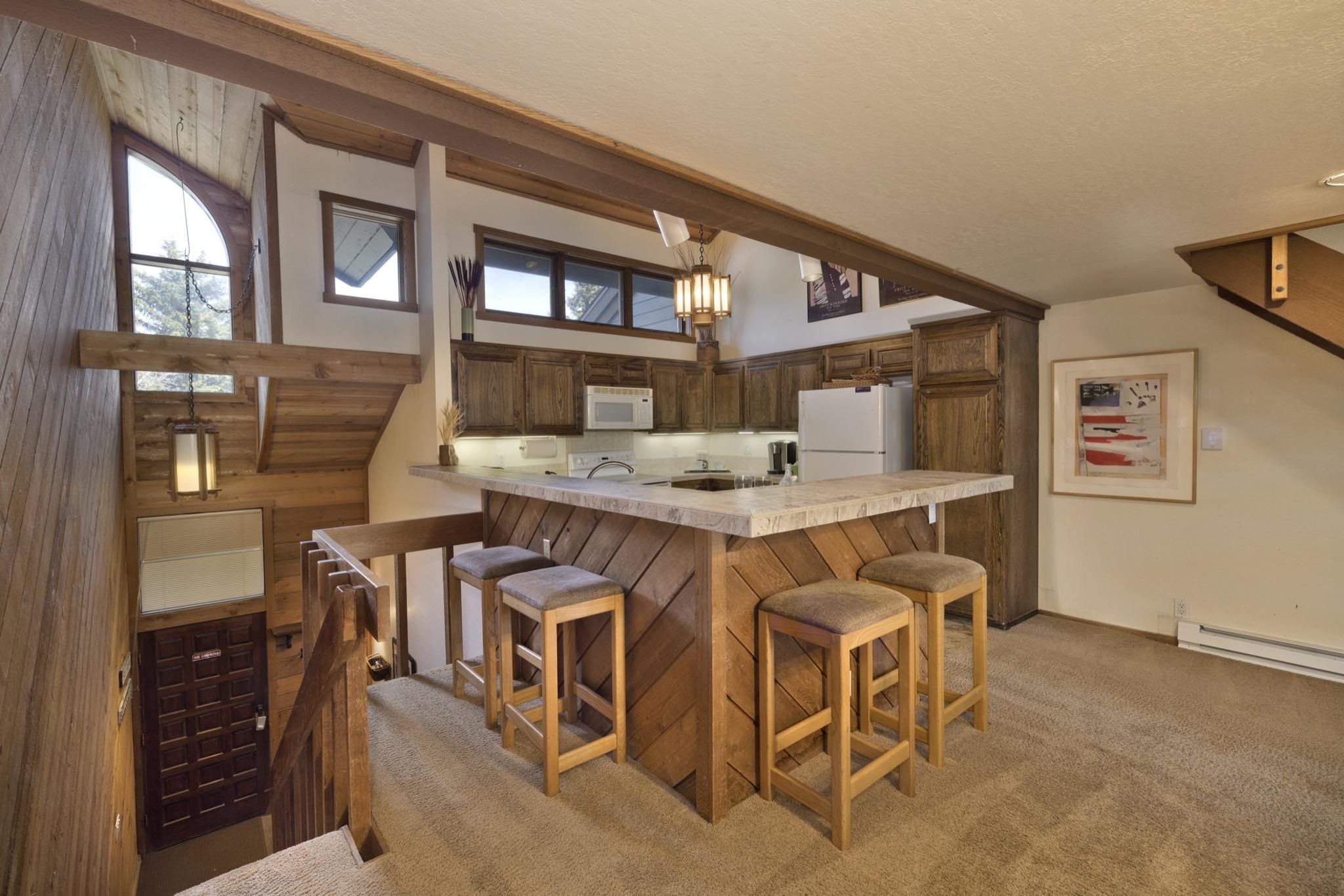 417 Snowcreek Road, Unit 417 Mammoth Lakes, CA 93546 - Photo 11 of 31 Kitchen with wood-finish cabinetry, white appliances, and a breakfast bar featuring a light-toned countertop and wood paneling