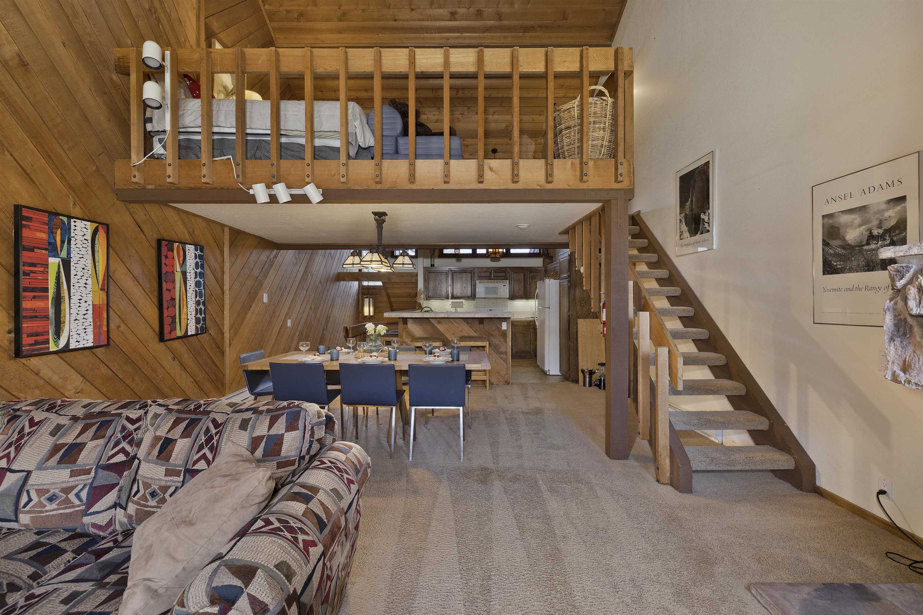 417 Snowcreek Road, Unit 417 Mammoth Lakes, CA 93546 - Photo 12 of 31 Open concept living area featuring a wood-paneled accent wall, a lofted space with wooden railing, a dining area with pendant lighting, and a staircase with carpeted treads