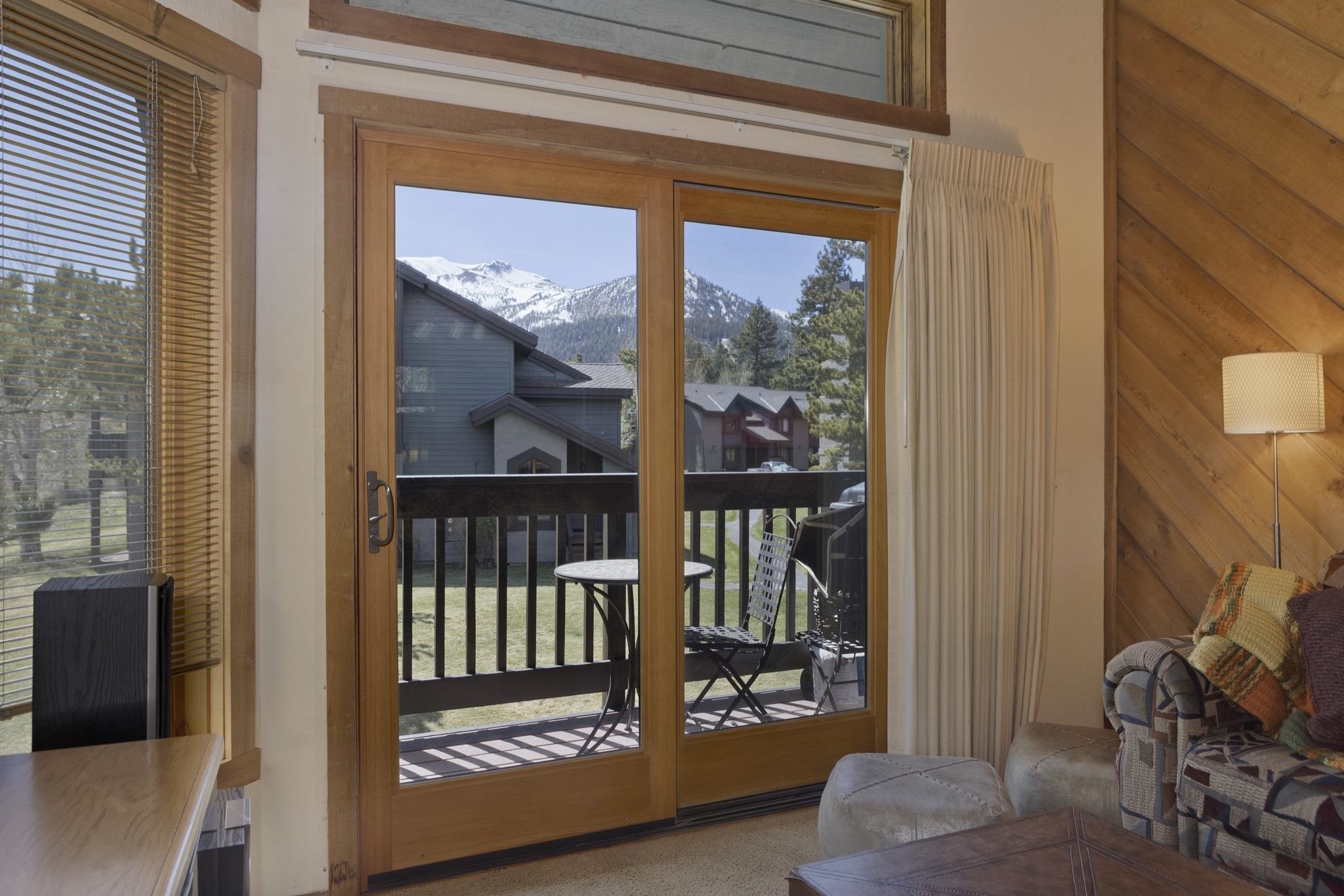 417 Snowcreek Road, Unit 417 Mammoth Lakes, CA 93546 - Photo 14 of 31 Wood-frame sliding glass doors open to a private balcony with a black railing, overlooking a green landscape and distant snow-capped mountains