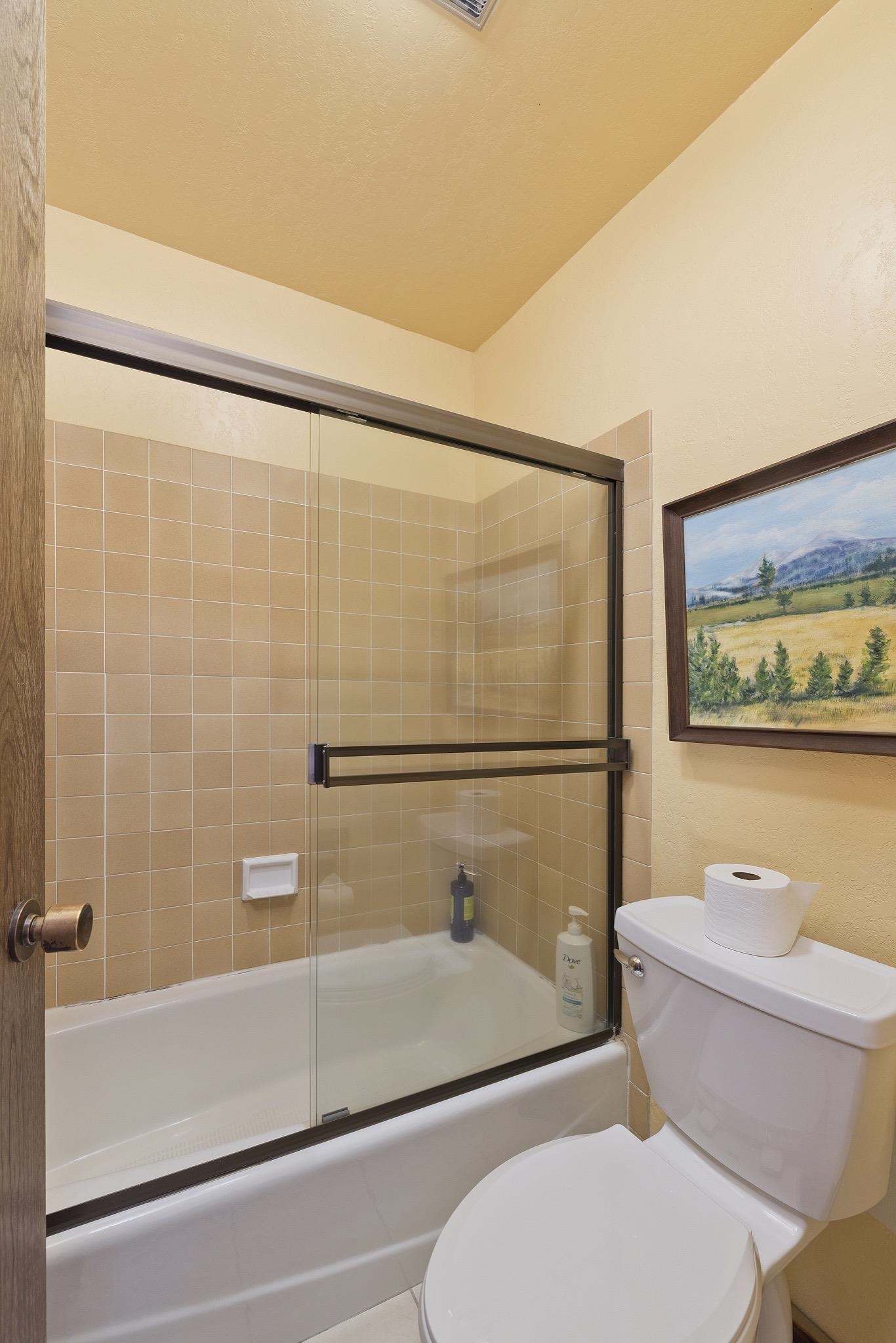 417 Snowcreek Road, Unit 417 Mammoth Lakes, CA 93546 - Photo 22 of 31 Bathroom featuring a white bathtub with sliding glass doors, tan square wall tiles, and a white toil