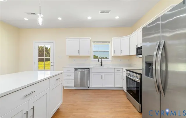 a kitchen with stainless steel appliances kitchen island granite countertop a refrigerator a sink a stove and white cabinets