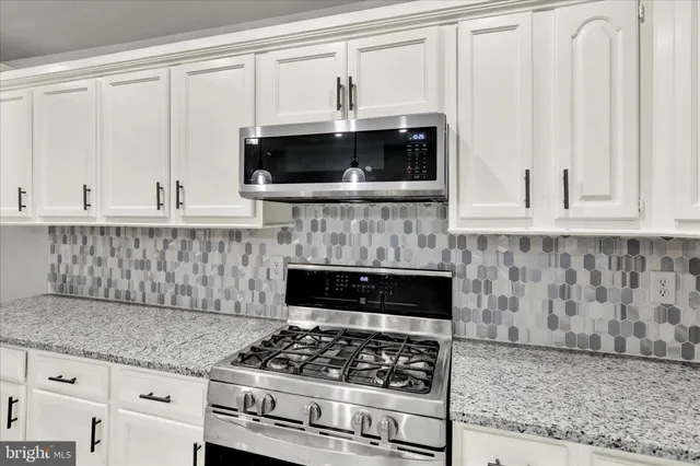 a kitchen with granite countertop a stove and a white cabinets