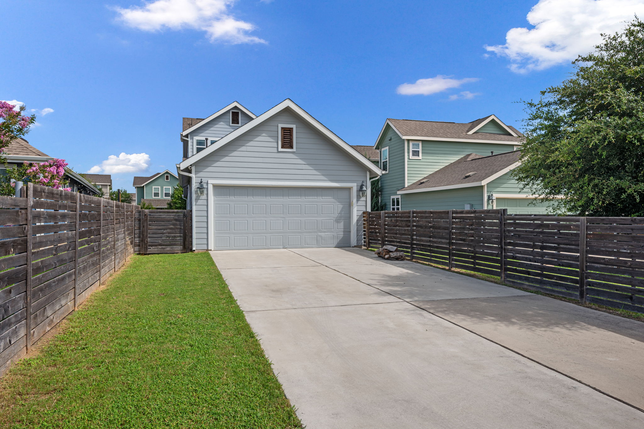 5409 Fox Wing Way Austin, TX 78747 - Photo 23 of 26 A spacious concrete driveway leads to the attached garage, framed by sturdy wood fencing and a patch of green lawn.