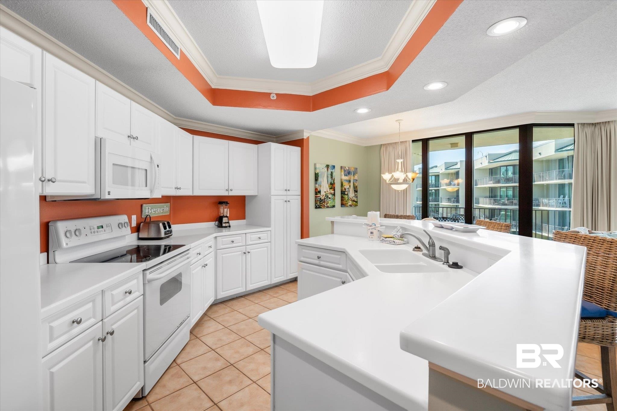 27580 Canal Road, Unit 1423 Orange Beach, AL 36561 - Photo 6 of 34 Kitchen with crown molding, light countertops, white appliances, a raised ceiling and recessed lighting.